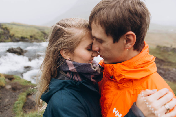 Vista ritagliata della giovane coppia che si abbraccia in una giornata cupa sullo sfondo della cascata
 - Foto, immagini