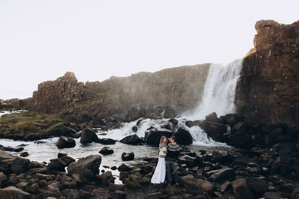 Pretty woman with long hair holding boyfriends elbow on waterfall background - Zdjęcie, obraz
