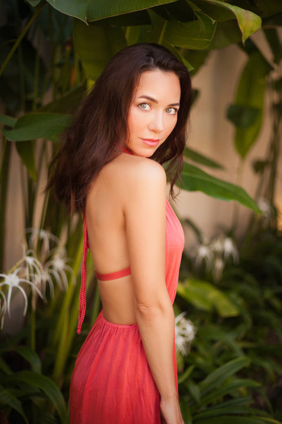 beautiful young woman in dress in front of tropical plants looking at camera - Foto, Imagen
