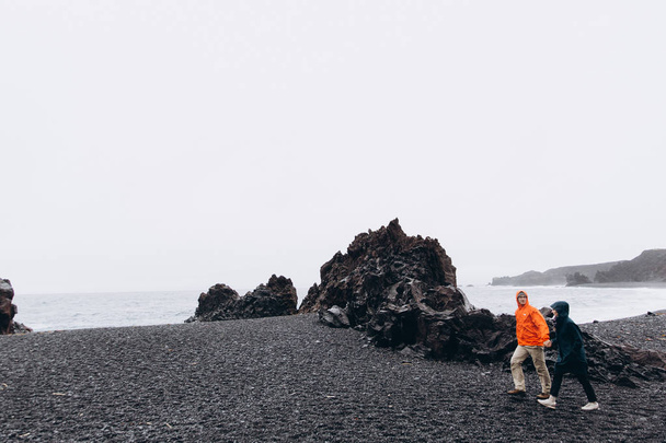 冷たい雨の日の海岸で歩いてレインコートを着て若いカップル - 写真・画像