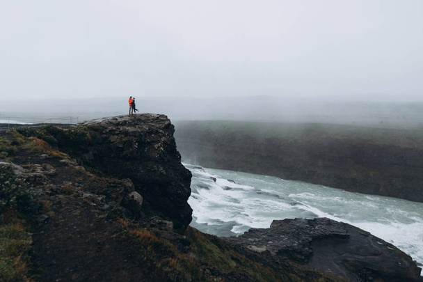 Young couple standing on cliff in gloomy day - Photo, Image