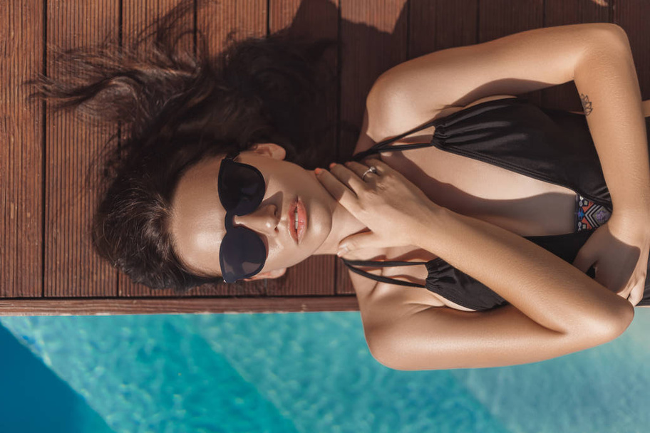 top view of attractive young woman in black swimsuit lying at poolside - Foto, Imagem
