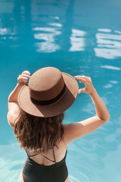 mooie jonge vrouw in badpak en stijlvolle hoed bij zwembad - Foto, afbeelding