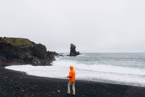 Вид сбоку на человека, идущего по берегу в холодный дождливый день
 - Фото, изображение