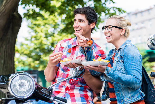 Τουριστική ζευγάρι παίρνει το υπόλοιπο κατά τη διάρκεια περιοδείας σκούτερ τρώει currywurst - Φωτογραφία, εικόνα