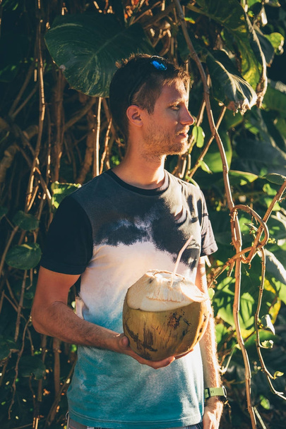 若い男ジャングル開催に立って、彼の手で新鮮なココナッツの飲み物. - 写真・画像