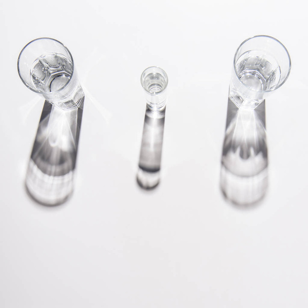 Hochwinkelaufnahme von verschieden großen Gläsern mit Wasser auf weißem Tisch - Foto, Bild