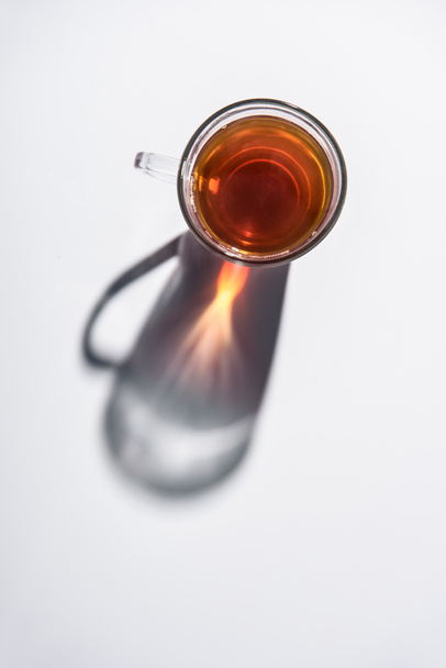 bovenaanzicht van glas cup met zwarte thee op witte tafel - Foto, afbeelding