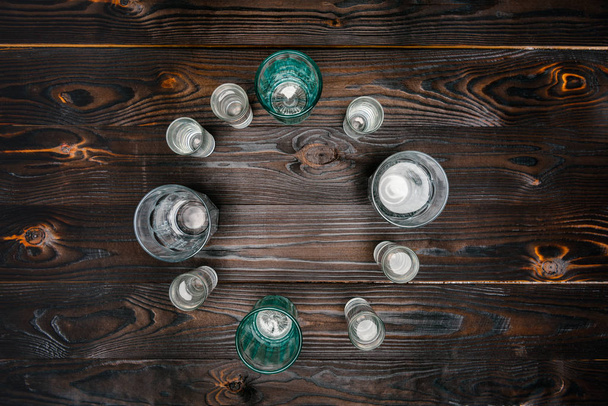 top view of circle with different sized glasses with water on wooden table - Φωτογραφία, εικόνα