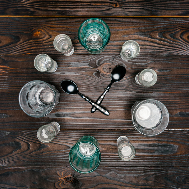 top view of circle with different sized glasses with water and spoons on wooden table - Foto, Imagen