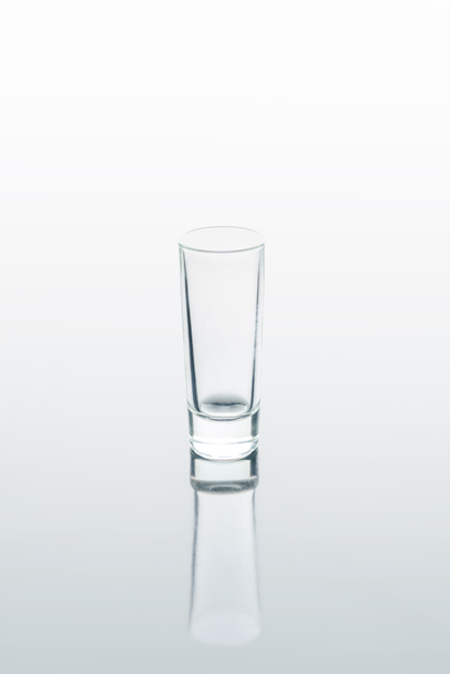een klein glas op wit reflecterend oppervlak - Foto, afbeelding