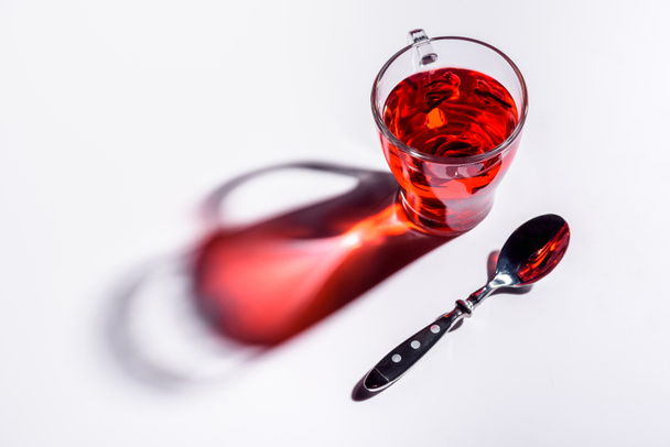 high angle view of glass cup with hibiscus tea and spoon on white table - Fotó, kép