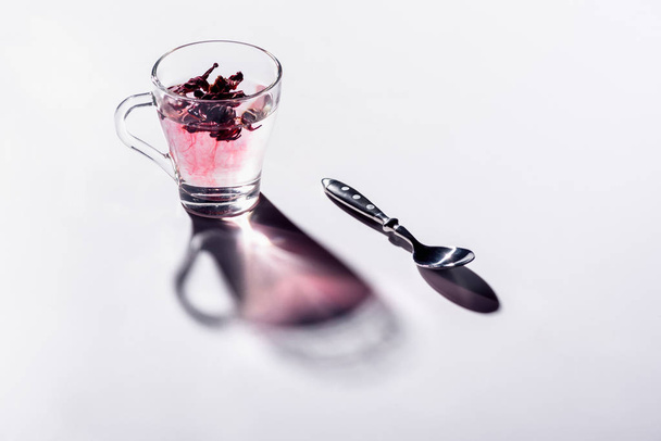 glazen kopje hibiscus thee met lepel op witte tafel - Foto, afbeelding