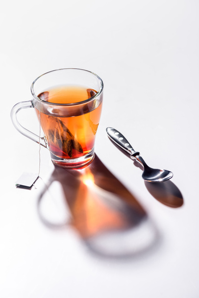 glazen kopje zwarte thee en lepel op tafel - Foto, afbeelding