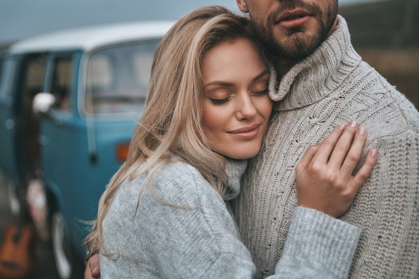 Beautiful young couple embracing near blue retro style mini van, woman Feeling protected - Foto, afbeelding