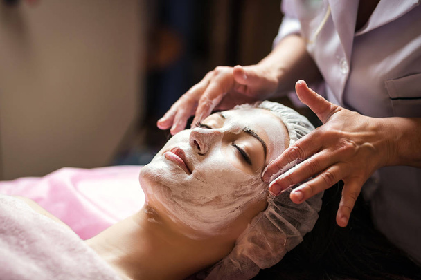 vrouw krijgt Gelaatsverzorging peeling masker door schoonheidsspecialiste op spa salon - Foto, afbeelding