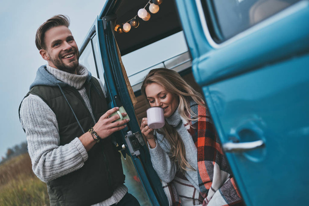 Beautiful young couple having hot drinks and smiling while enjoying their road travel - Фото, изображение
