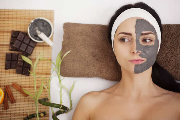 Wellness massage voor jonge vrouw met gezichts masker op gezicht - binnenshuis - Foto, afbeelding