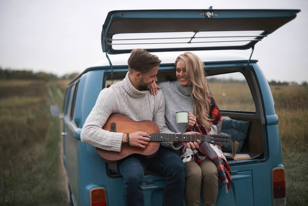 handsome man playing acoustic guitar for his beautiful blonde girlfriend - Фото, изображение