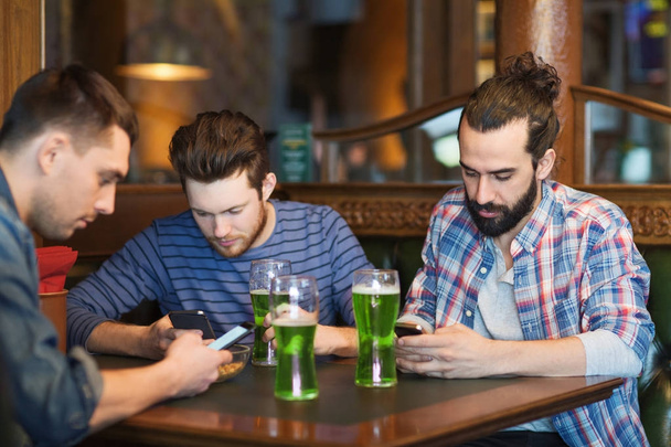 friends with smartphones and green beer at pub - Photo, image