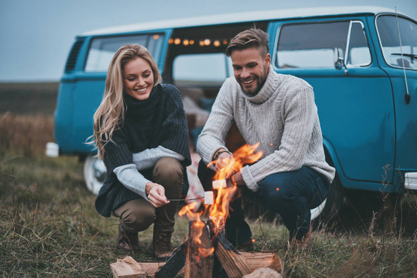 Beautiful young couple roasting marshmallows over a campfire  - Fotó, kép