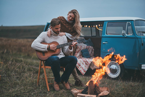 Handsome young man playing guitar for his attractive girlfriend while sitting by the bonfire - 写真・画像