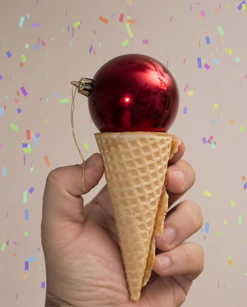 Szczęśliwego nowego roku. męskiej ręki trzymającej stożek lody z czerwone okrągłe świąteczne zabawki, ozdoba, na białym tle   - Zdjęcie, obraz