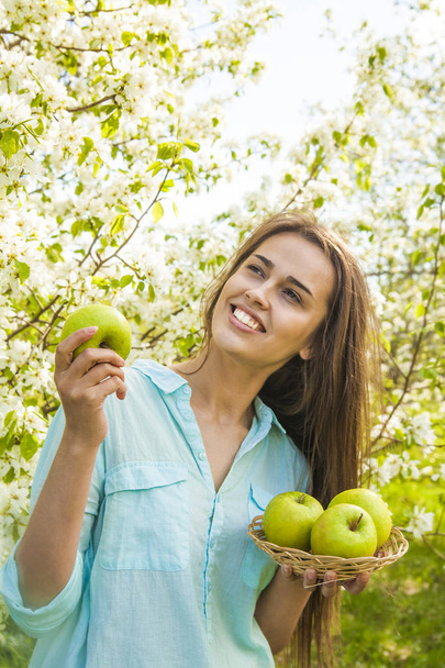  young beautiful woman holding apples against blooming apple tree background  - Valokuva, kuva