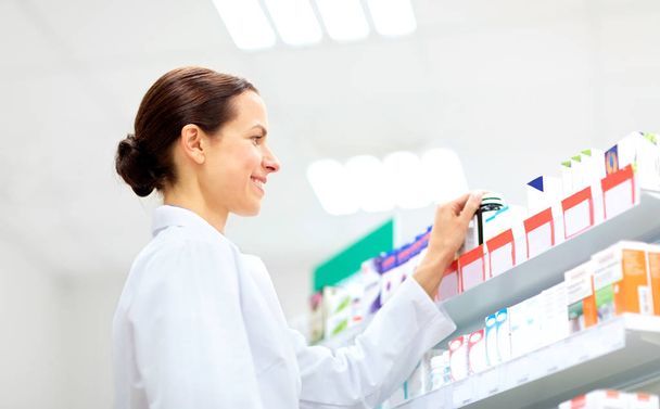 happy female apothecary with drug at pharmacy - Foto, afbeelding