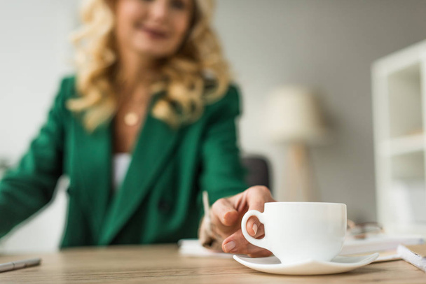 primo piano vista parziale della donna d'affari che tiene una tazza di caffè sul posto di lavoro
 - Foto, immagini