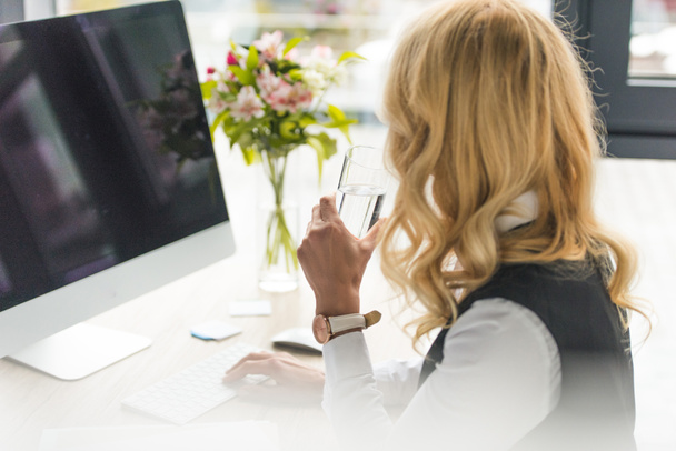 enfoque selectivo de la mujer de negocios sosteniendo un vaso de agua y el uso de computadora de escritorio en el lugar de trabajo
  - Foto, imagen