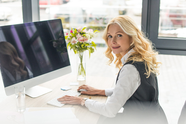 businesswoman using desktop computer and looking at camera at workplace - Fotó, kép