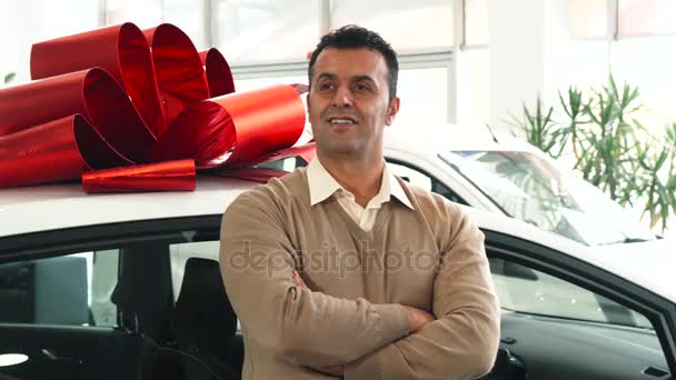 Egy szilárd férfi áll a háttérben egy autó-val egy ajándék íj - Felvétel, videó