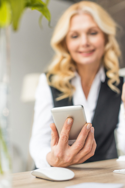 close-up view of smiling middle aged businesswoman using smartphone - Zdjęcie, obraz