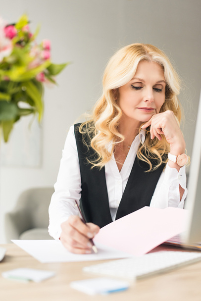 selective focus of middle aged businesswoman doing paperwork at workplace - Fotografie, Obrázek