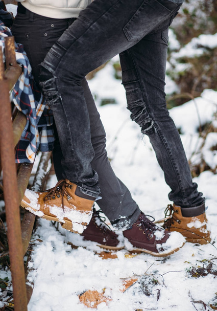 legs of the young girl stand opposite to legs of the young man, lovers. Snow background. Fashion shoes and dark grey jeans - Fotó, kép