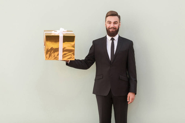 smiling boss holding gold gift box on gray background  - Foto, Imagen