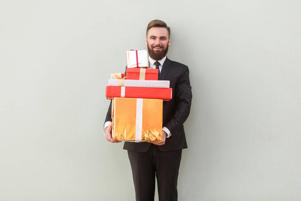 счастливый улыбающийся бизнесмен держит красочные подарочные коробки на сером фоне
 - Фото, изображение