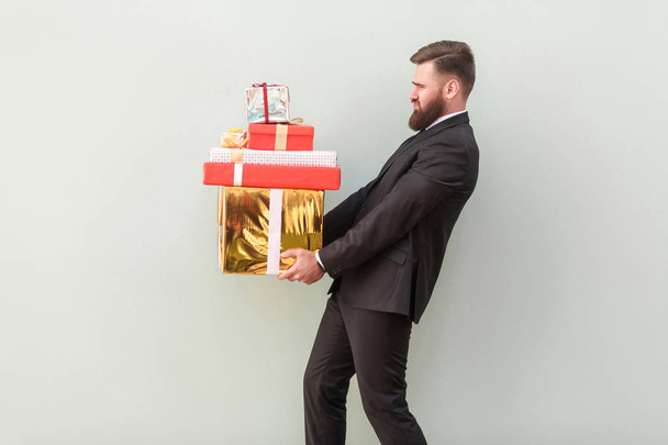 tired boss holding pile of heavy gift boxes on grey background  - 写真・画像
