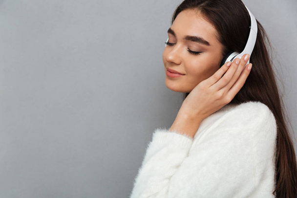Side view of happy brunette woman in sweater and headphones - Photo, image