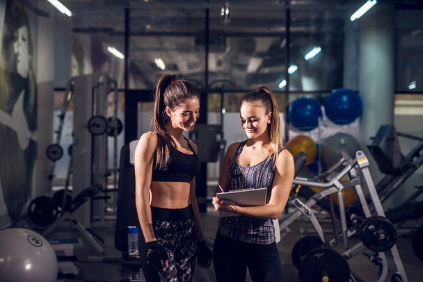 junge schlanke Frau berät sich mit hübscher Personal Trainerin im Fitnessstudio - Foto, Bild