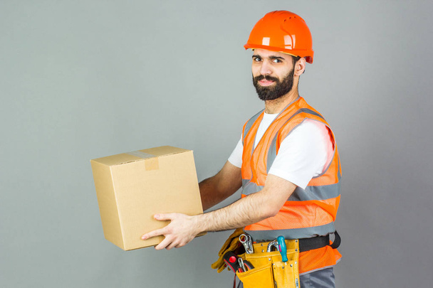 A man-builder in an orange helmet with a cardboard box in his ha - Zdjęcie, obraz