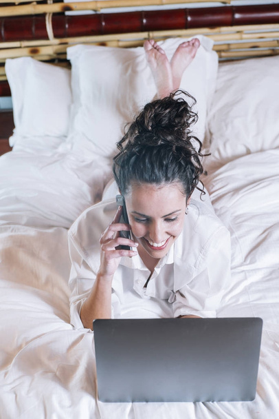 Mujer bonita con teléfono y portátil en la cama
 - Foto, imagen