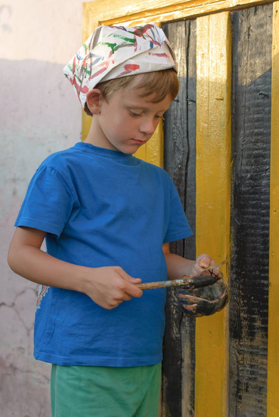 A fiú végez egy festmény az ajtó festése a szabadban nyáron szabadban. Helyreállítása érdekében, és javítja a megjelenését az épület. Dips az ecset, a festék jar. - Fotó, kép