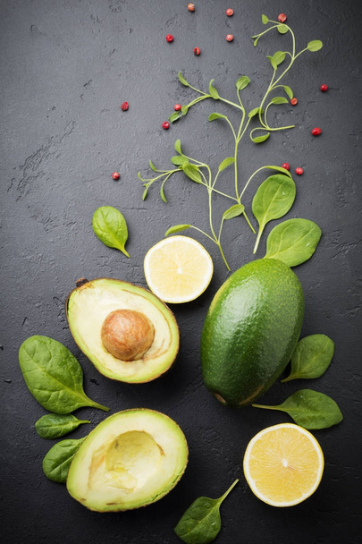 Food background with green vegetables: avocado, spinach, chavran leaves, red pepper and lemon on a dark black old slate, stone or concrete background. Selective focus. Top view.Space for text. - Photo, image