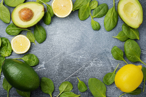 Food background with green vegetables: avocado, spinach and lemon on a dark old slate, stone or concrete background. Selective focus.Top view. Space for text. - Foto, imagen