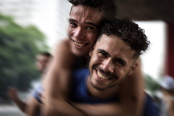 Homoseksuaalinen pari syleilee ja katsoo kameraa
 - Valokuva, kuva