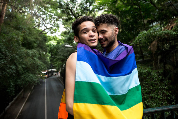 Homopariskunta syleilee sateenkaaren lippua puistossa
 - Valokuva, kuva