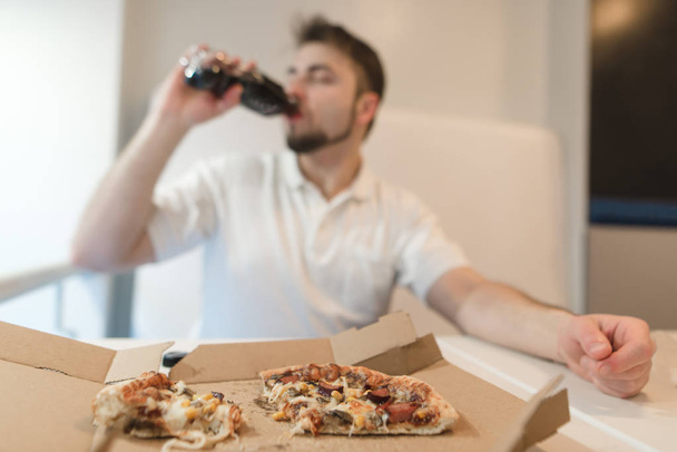 Um homem bebe uma garrafa depois de beber um fast food. Beba depois da pizza. Foco na pizza
. - Foto, Imagem