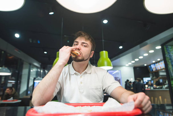 Człowiek siedzi przy stoliku w kawiarni i zjada pyszne kanapki. Przekąska w restauracji fast food. - Zdjęcie, obraz